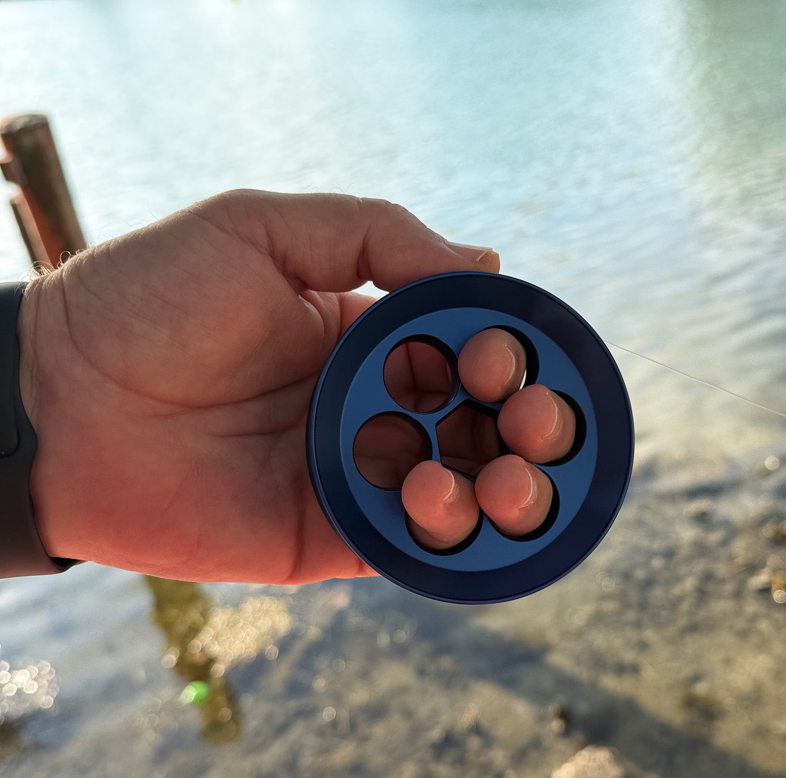 Hand holding a blue hand line fishing reel  against a blurred natural background