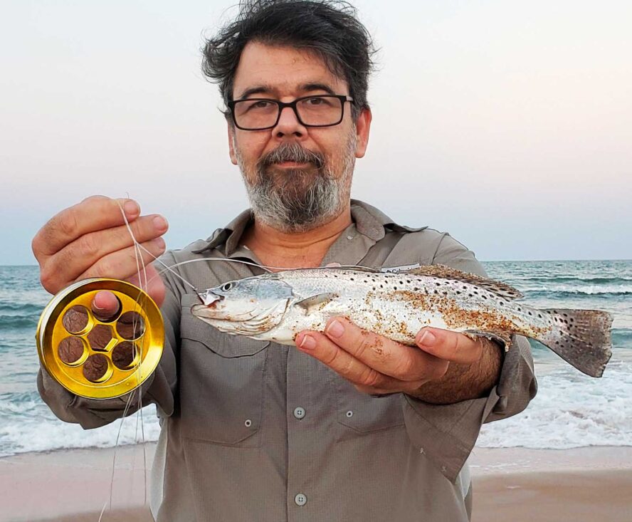 Man with hand line fishing reel on one hand and a fish on the other one