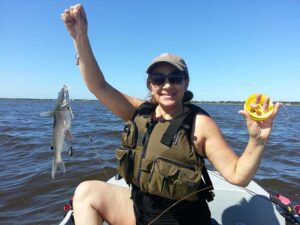 Woman sitting on kayak with a fish on one hand and a hand line reel on the other one