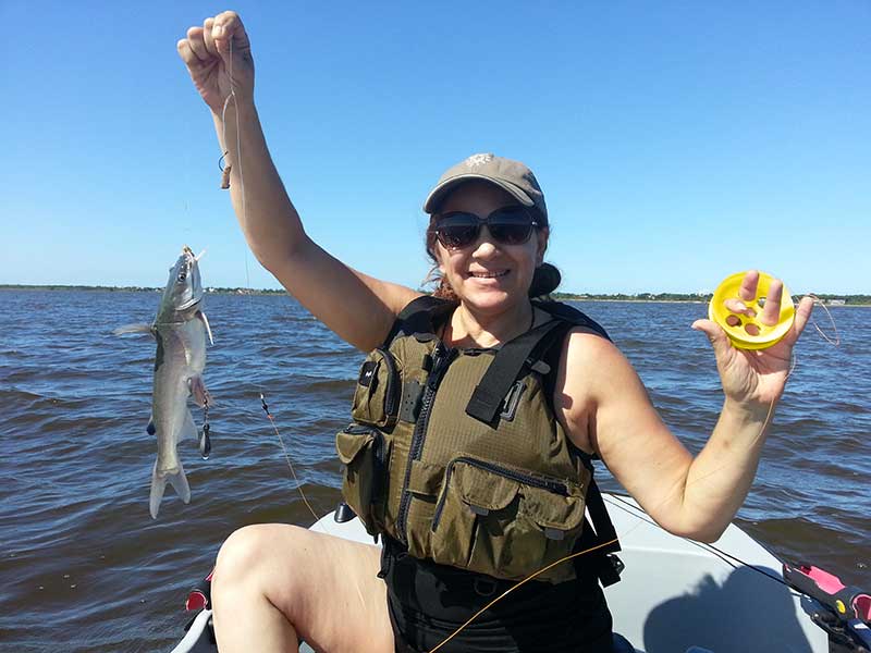 Woman sitting on kayak with a fish on one hand and a hand line reel on the other one